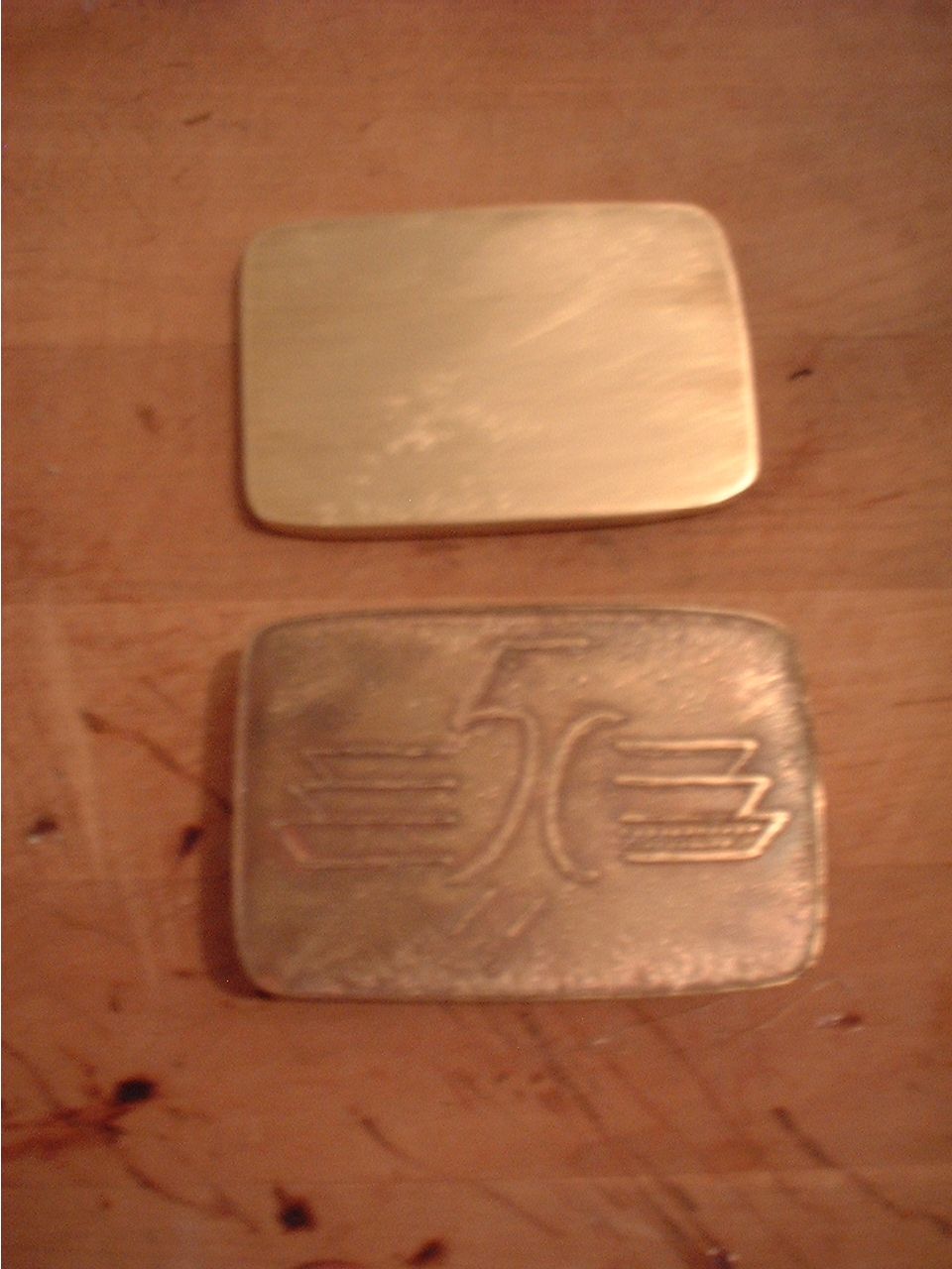 A polished buckle blank and one already etched.
